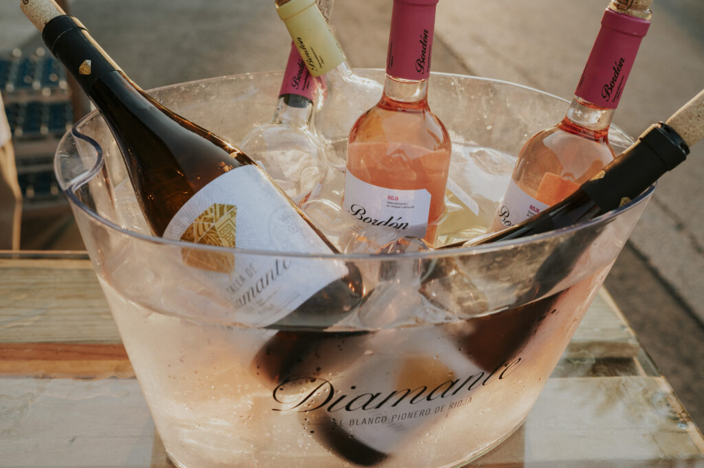 Primer plano de una gran hielera de plástico llena de hielo picado y agua, en la que se enfrían botellas de vino Diamante (blanco) y Bordón Rosado de Bodegas Franco-Españolas en un entorno de cine de verano en La Rioja.